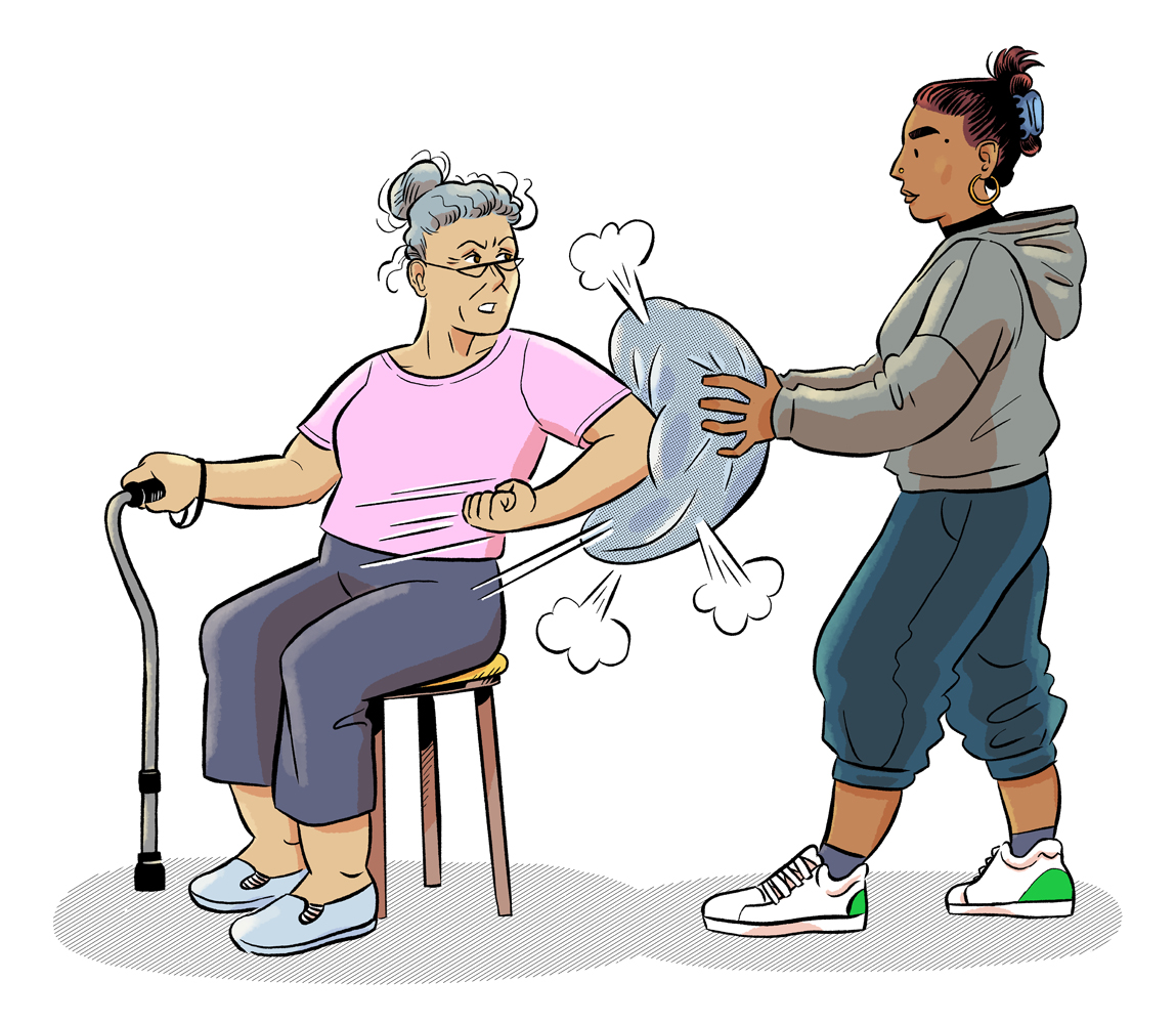 Une femme âgée assise frappe dans un coussin avec son coude, tenu par une autre personne